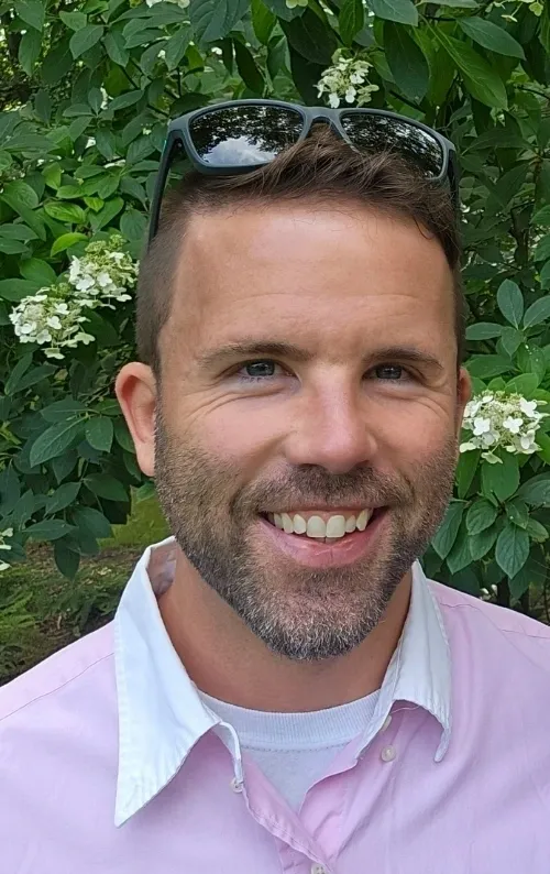 A man with a beard and sunglasses smiling for the camera.