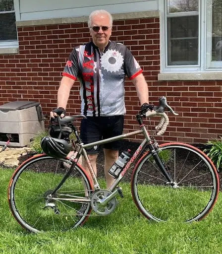 A man standing in the grass with his bike.