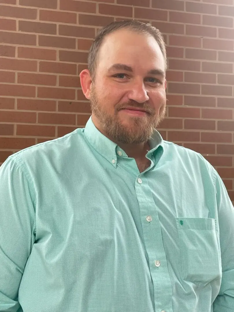 A man in a green shirt standing next to a brick wall.