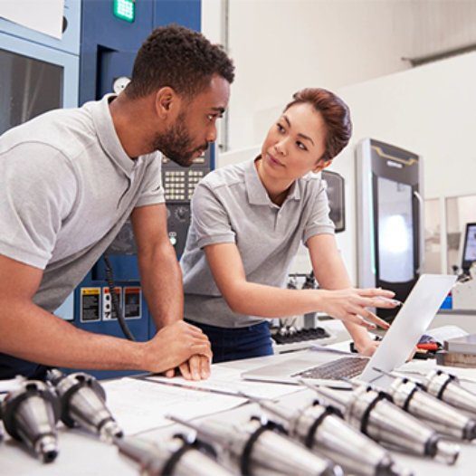 Two people looking at a laptop in front of machines.